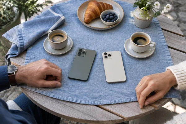 Illustratief beeld: twee omgekeerde telefoons, koffiekopjes en ontspannen handen op een blauw tafelkleed